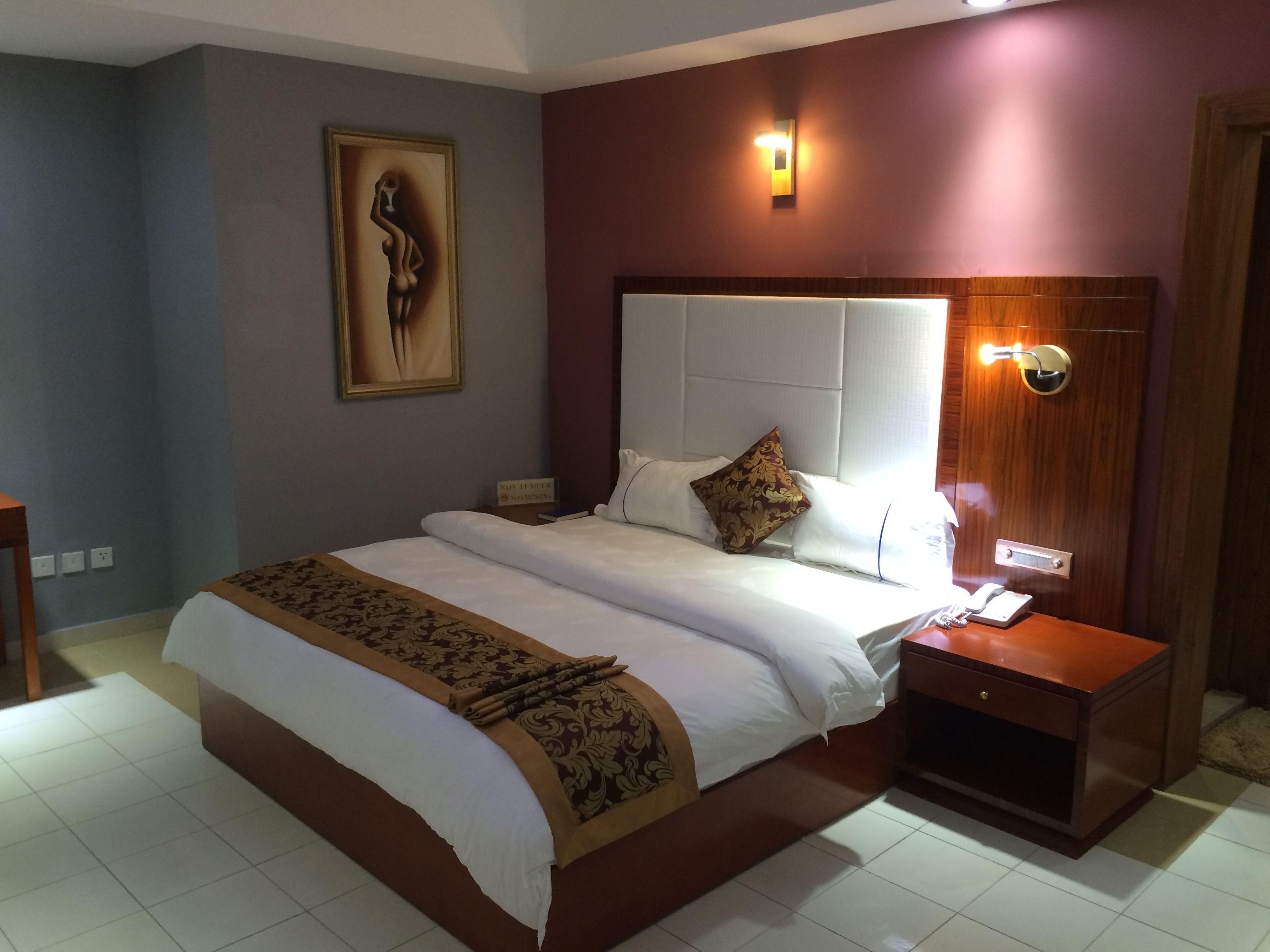 Una habitación de hotel con una cama grande, una mesita de noche, una lámpara de pared y un cuadro en la pared.
