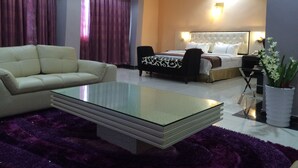 A hotel room with a bed, a sofa, a glass coffee table, and a potted plant. - Sun Beach Hotel (Cotonou)