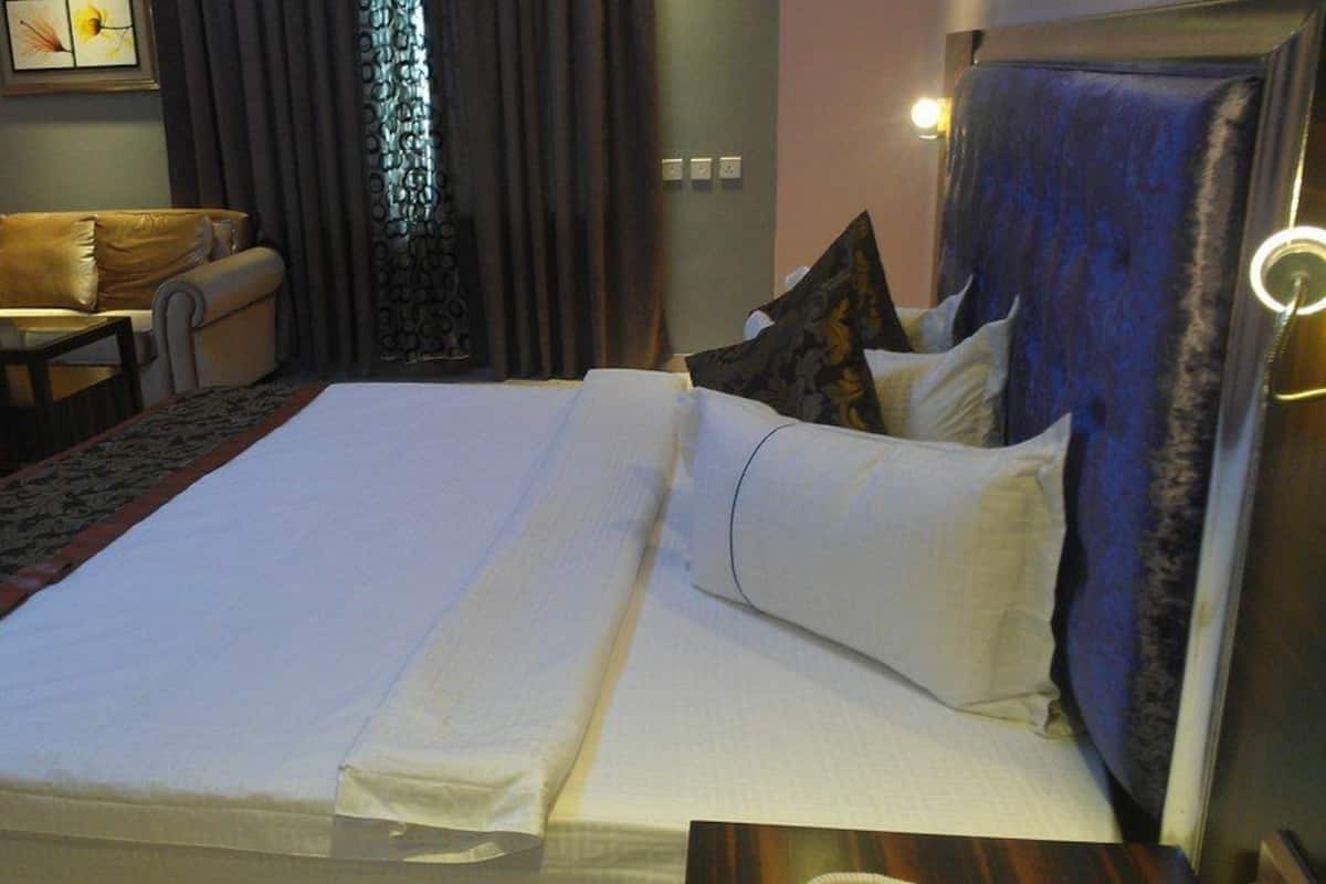 A neatly made bed with white linens and multiple pillows, a leather sofa, a small table, and a patterned rug.