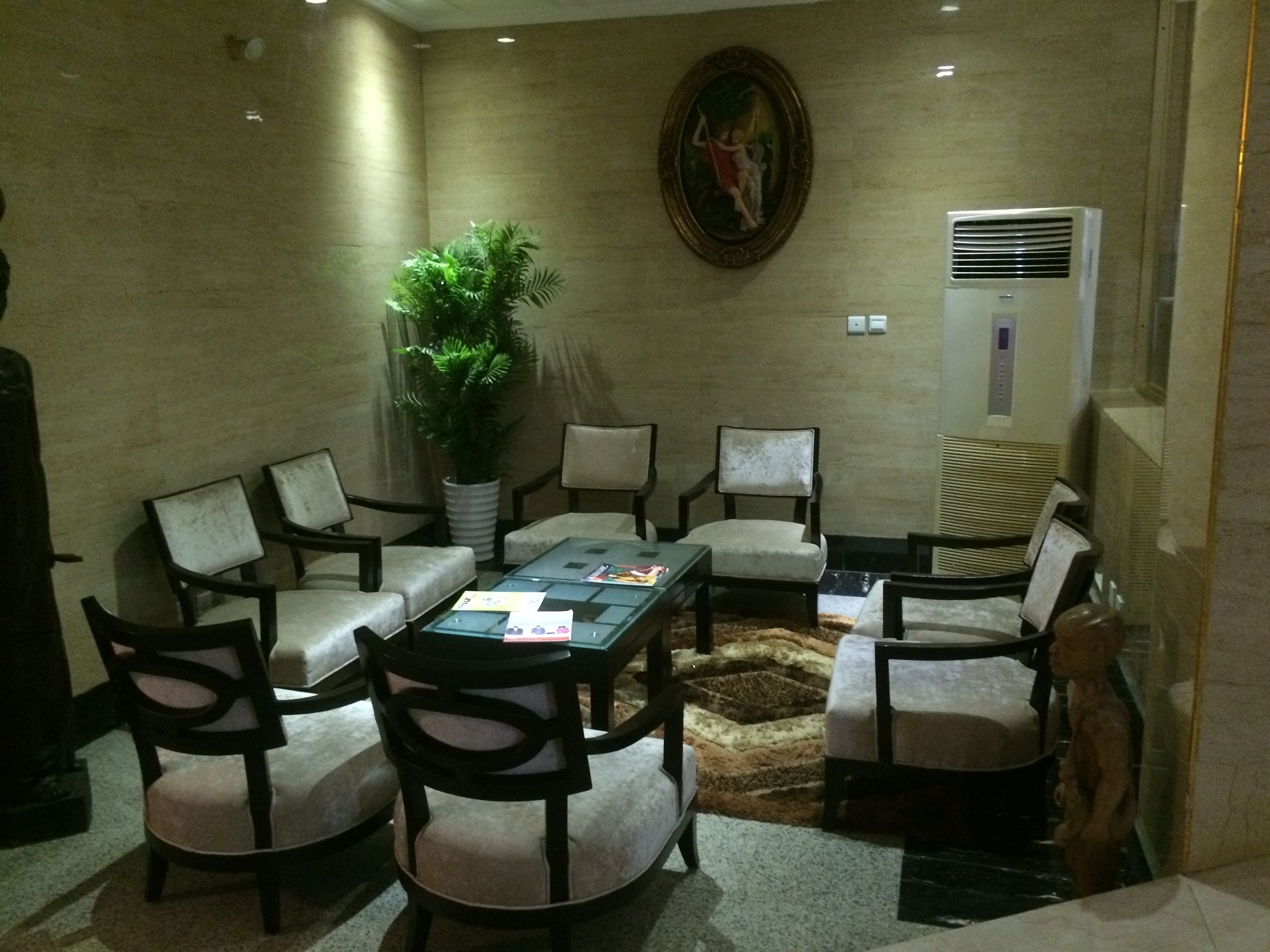 A conference room with a round table, six chairs, a potted plant, a painting, and an air conditioning unit.
