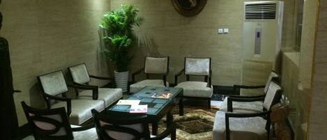 A conference room with a round table, six chairs, a potted plant, a painting, and an air conditioning unit.