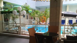 An indoor pool area with a view of the pool, surrounded by wicker chairs and tables, and a fire extinguisher visible in the background. - Sun Beach Hotel (Cotonou)
