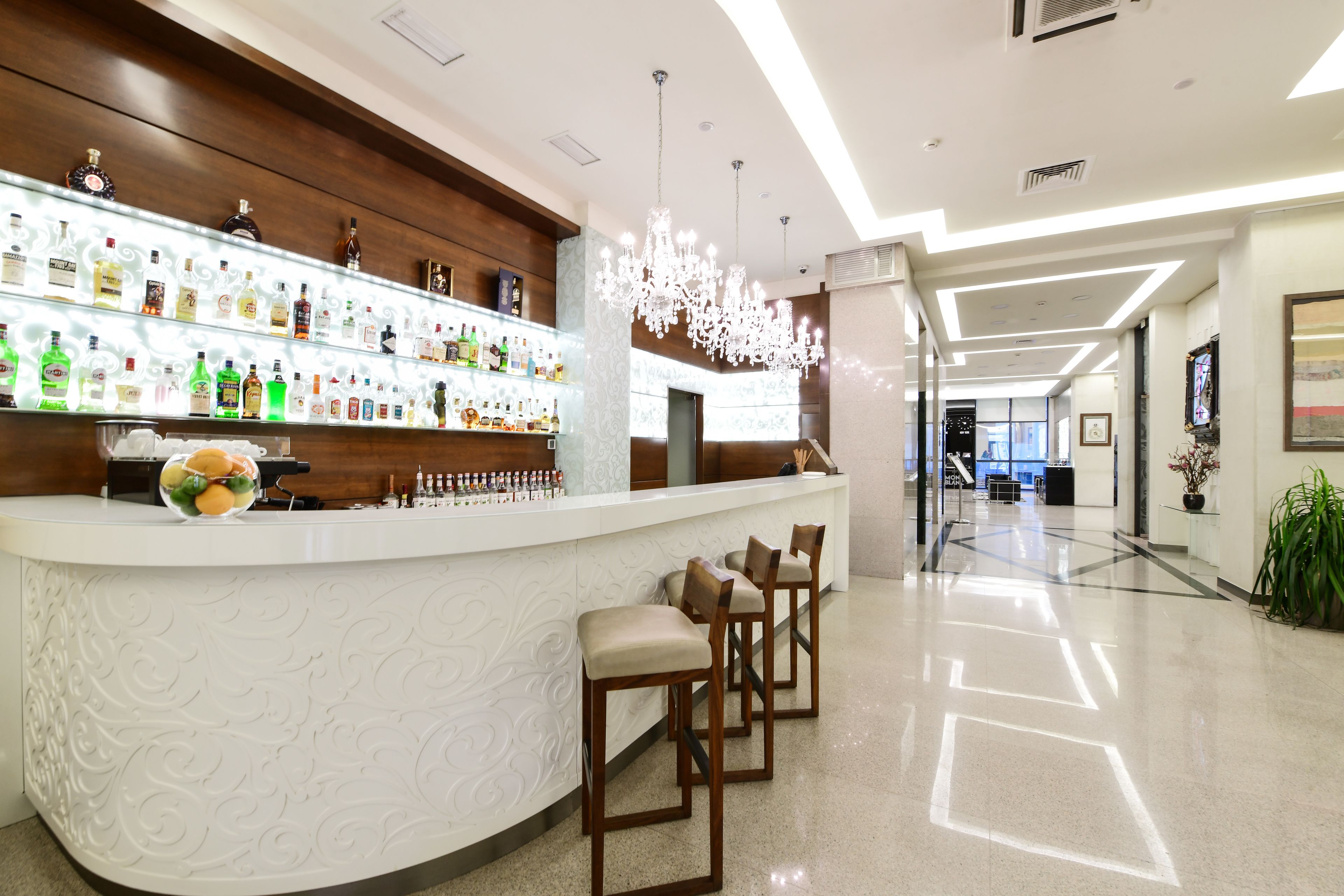 A modern bar area with a white countertop, multiple liquor bottles, and three wooden bar stools.