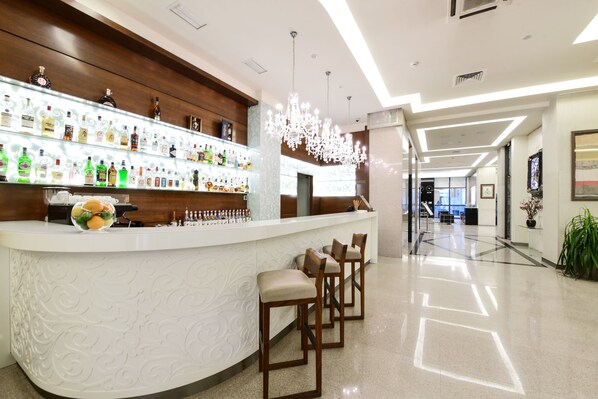 Un área de bar moderna con una encimera blanca, varias botellas de licor y tres taburetes de madera.