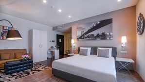 Ein modernes Hotelzimmer mit einem großen Bett, einem Sofa, einem Schreibtisch und einem Stadtbild an der Wand.