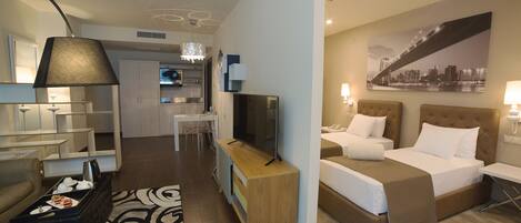 Una habitación de hotel con cama, escritorio, silla, televisor y kitchenette.