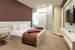Een moderne slaapkamer met een groot bed, een nachtkastje, een televisie en een badgedeelte met een douche.