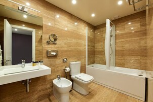 Een moderne badkamer met een hygiëneschuimer, toilet en bad.