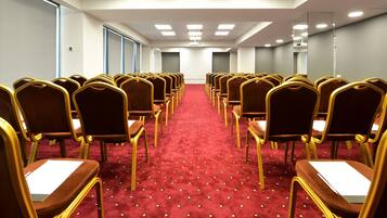 Un salón de conferencias con filas de sillas doradas y piso cubierto de alfombra roja.