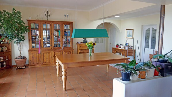A spacious dining area with a wooden table, surrounded by bookshelves and potted plants.