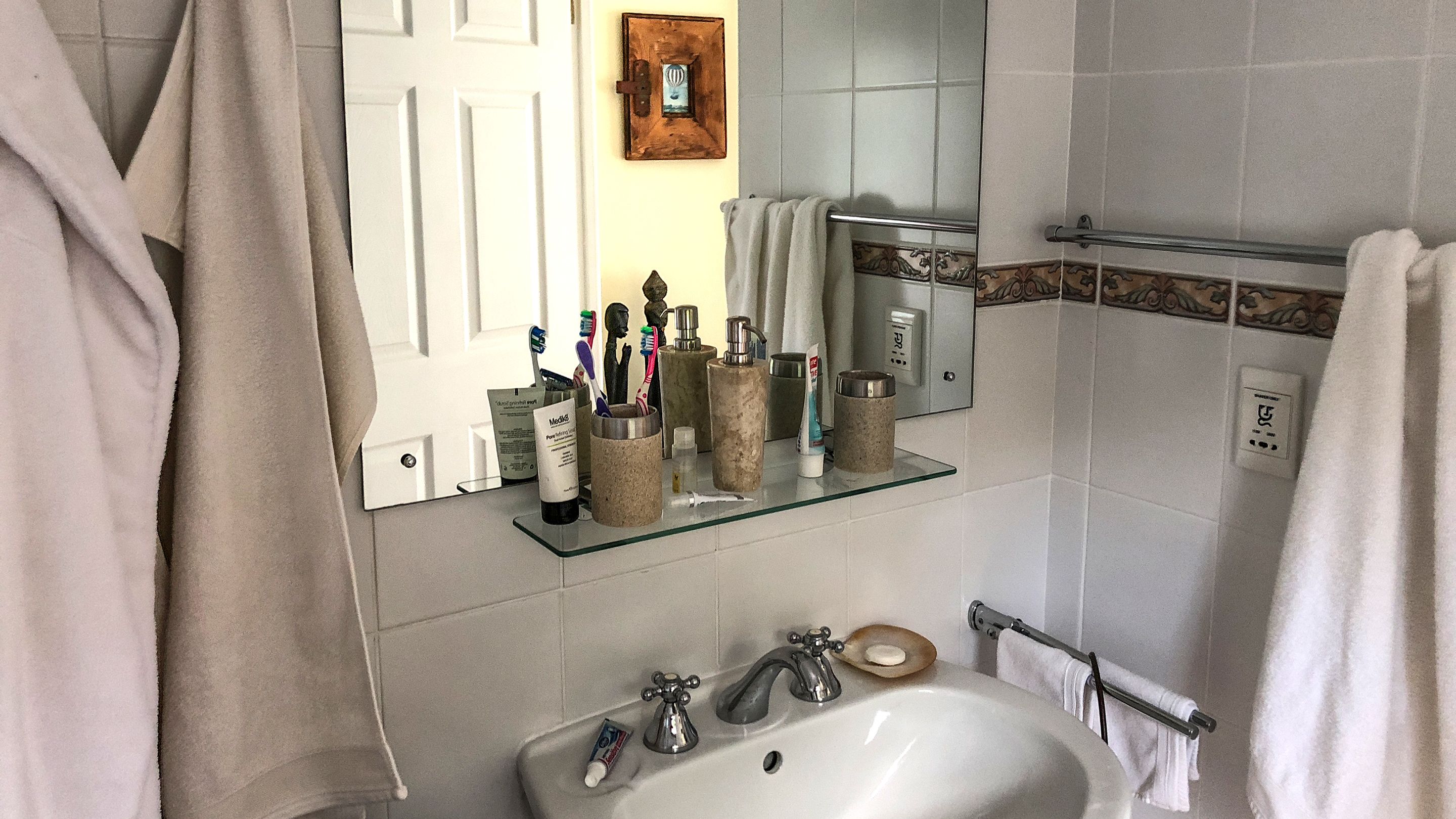 Un baño con lavamanos, dos grifos, un espejo y un perchero para toallas.