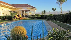 Ein Schwimmbad mit Terrassenbereich, umgeben von Grünflächen und Blick auf Berge.