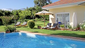 A pool area with lounge chairs, a covered patio, and a view of mountains. - Somerset Sights Bed and Breakfast (Cape Town)