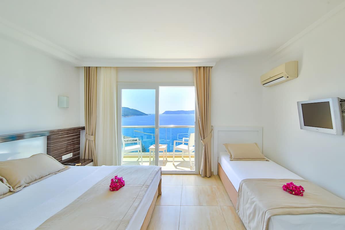 A hotel room with two beds, a TV, and a balcony with a view of the sea.