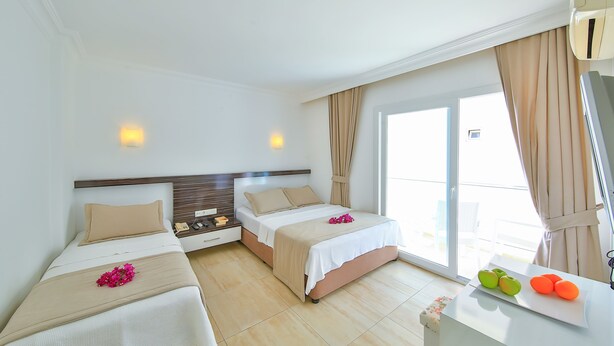 A hotel room with two beds, a large window with curtains, a small table with fruit, and a wall-mounted air conditioner. - Belinda Hotel (Kas)