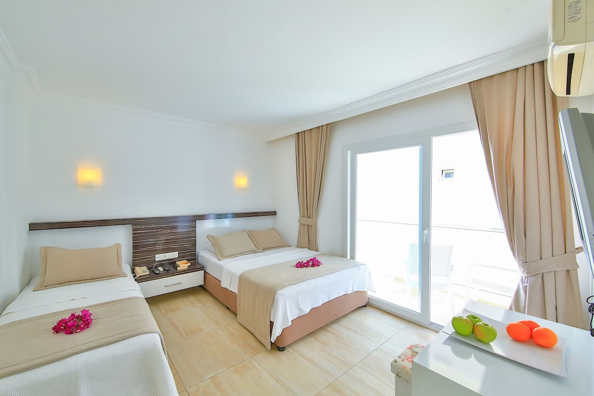 A hotel room with two beds, a large window with curtains, a small table with fruit, and a wall-mounted air conditioner.