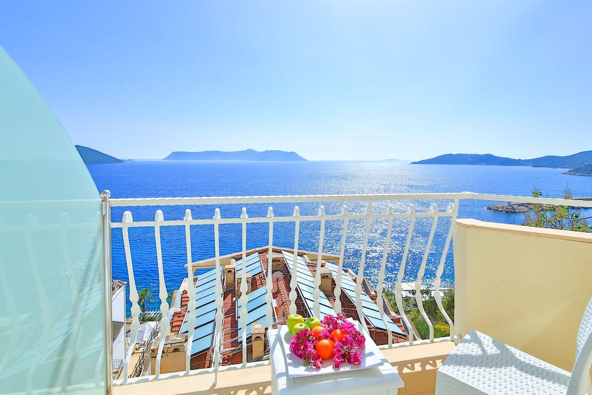 A balcony with a view of the sea, a table with fruit and flowers, and a white railing.
