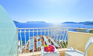 Un balcón con vistas al mar, una mesa con fruta y flores, y una barandilla blanca.