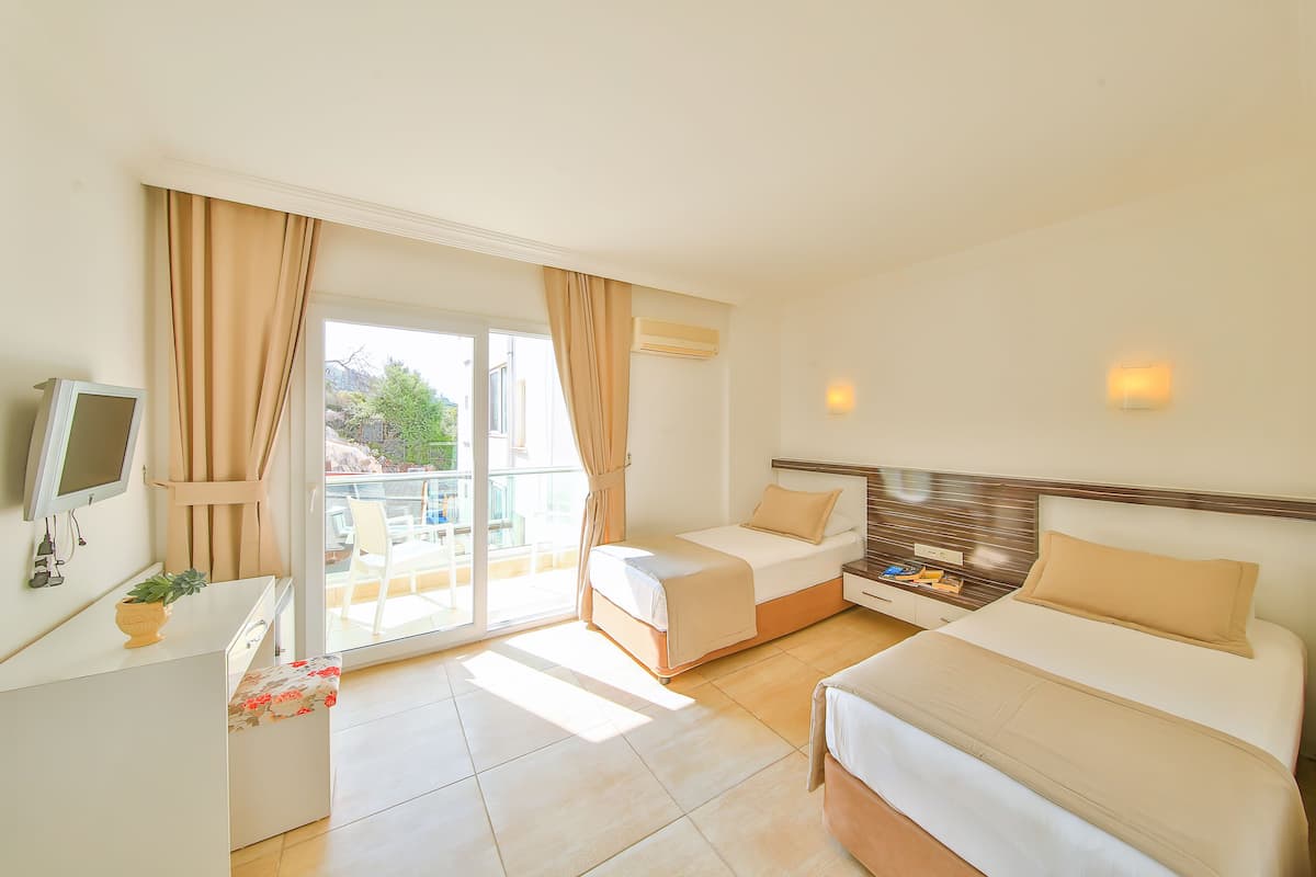 A hotel room with a bed, a desk, a TV, and a balcony with curtains.