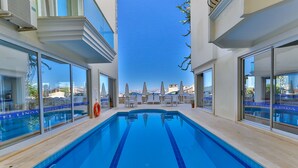 A swimming pool with clear blue water, surrounded by lounge chairs and umbrellas, with a view of buildings and a clear sky. - Belinda Hotel (Kas)
