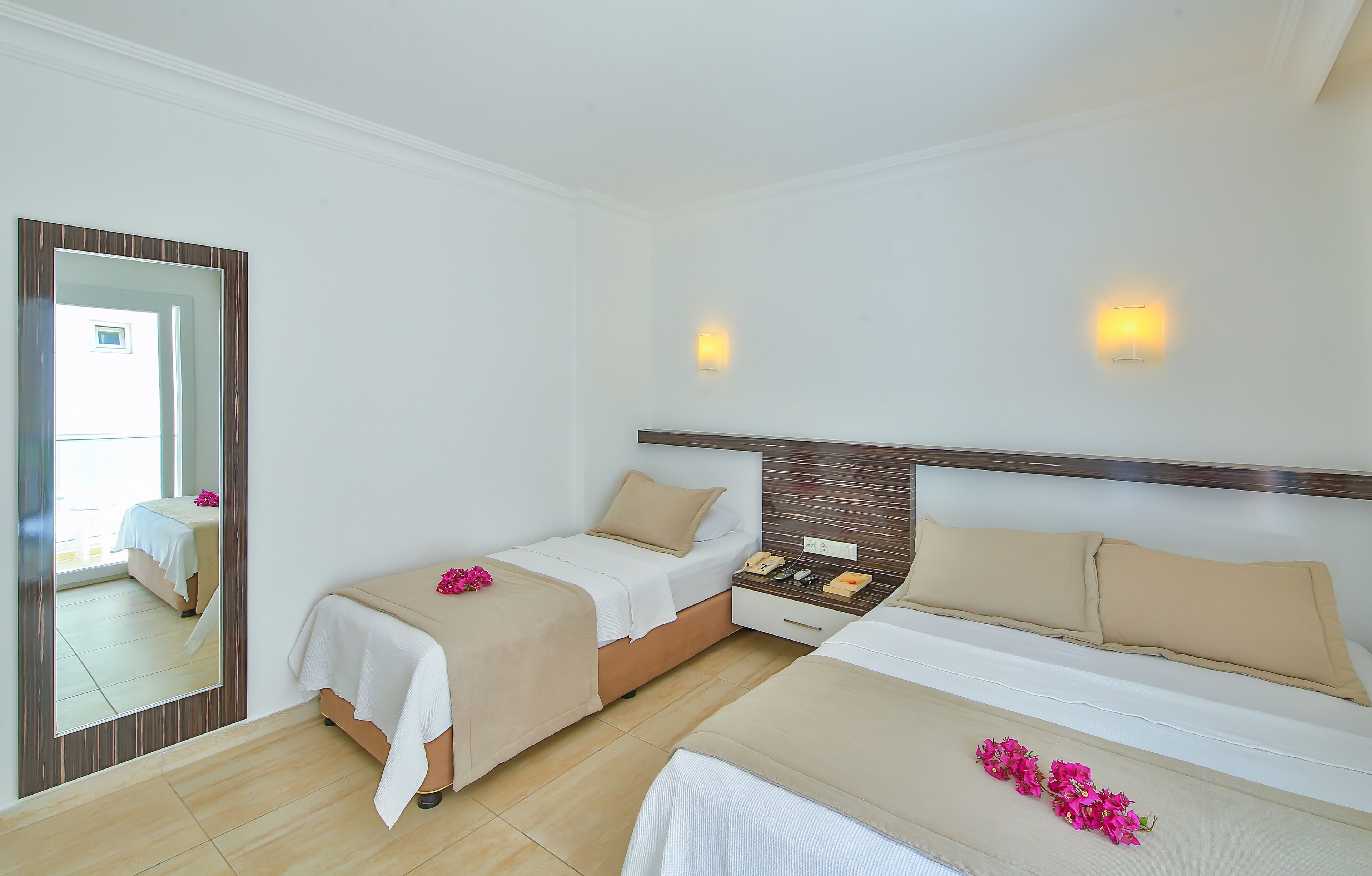 A hotel room with two beds, a large mirror, bedside lamps, and a small table with a phone and a notepad.