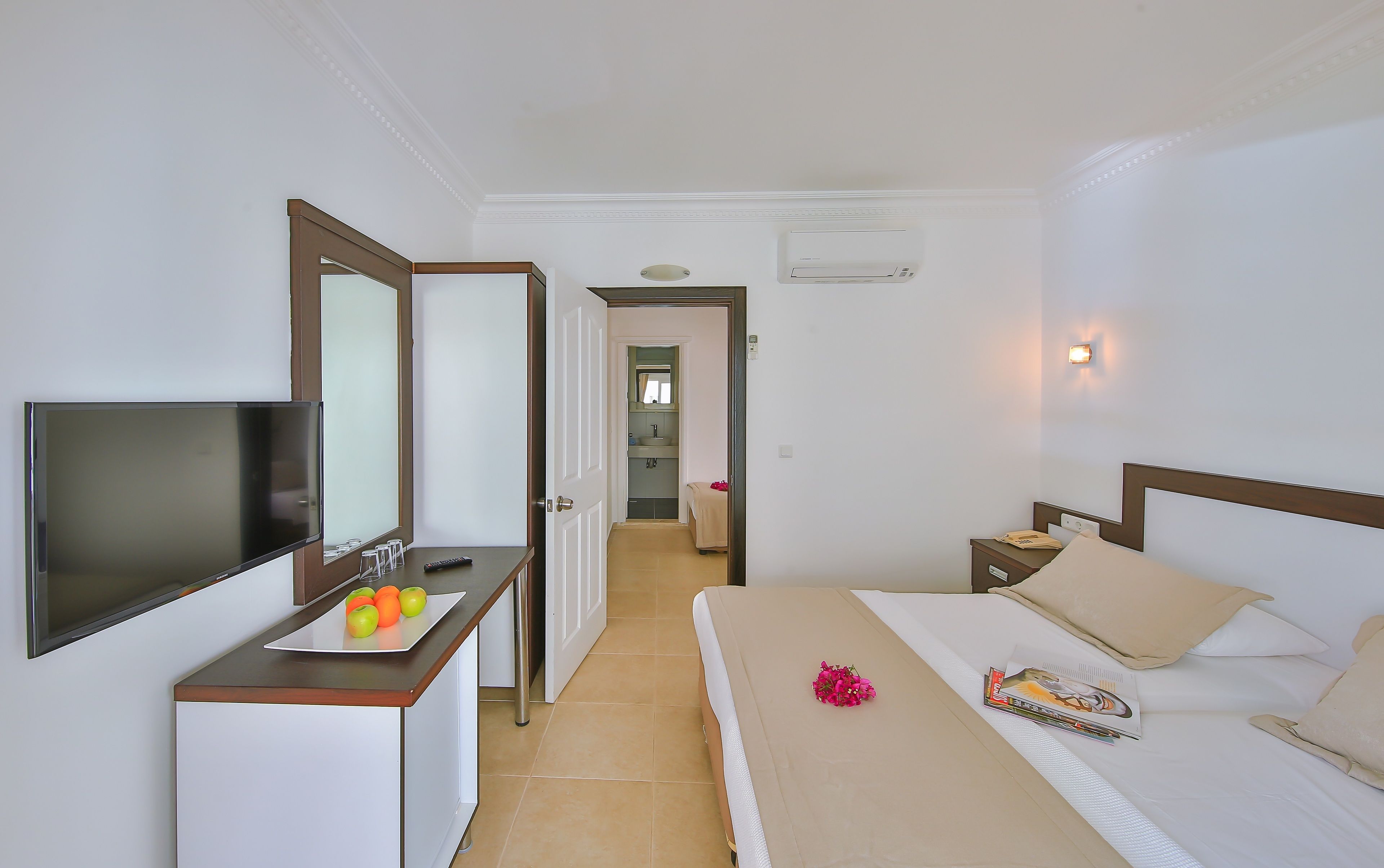 A hotel room with a bed, bedside table, TV, and a bathroom visible through an open door.