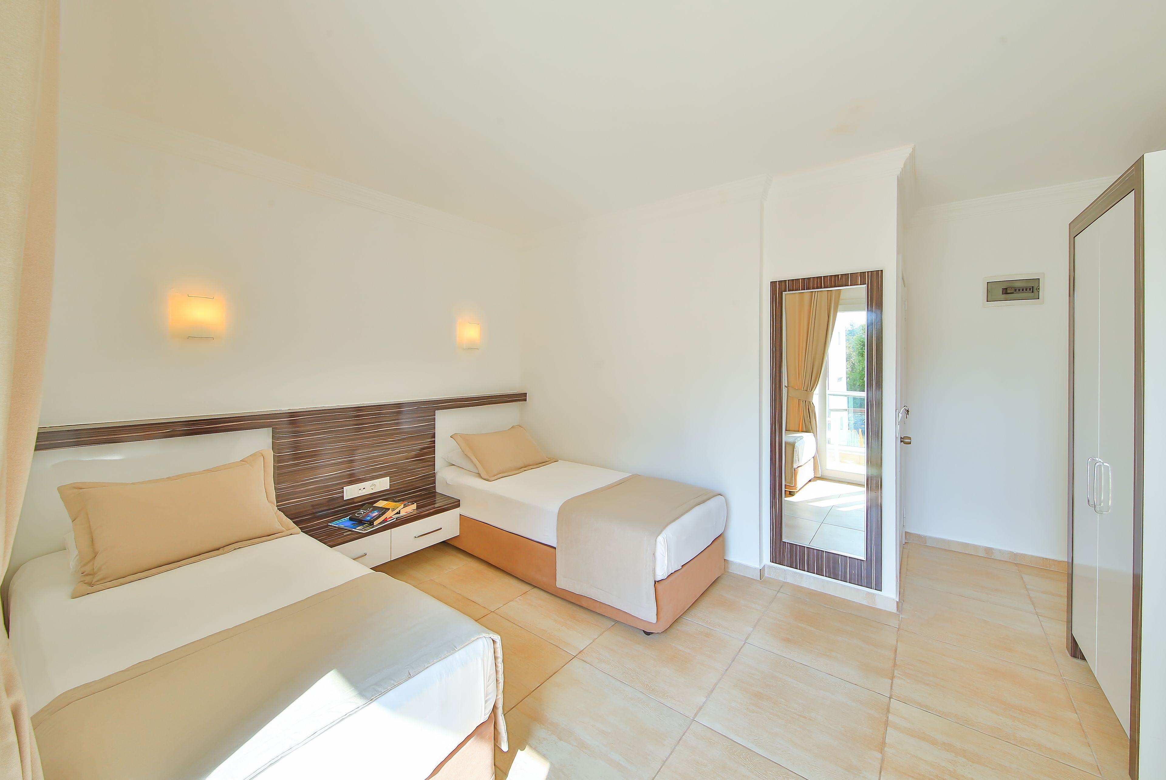 A hotel room with two beds, a wooden headboard, a small table with a chair, and a door leading to a balcony.