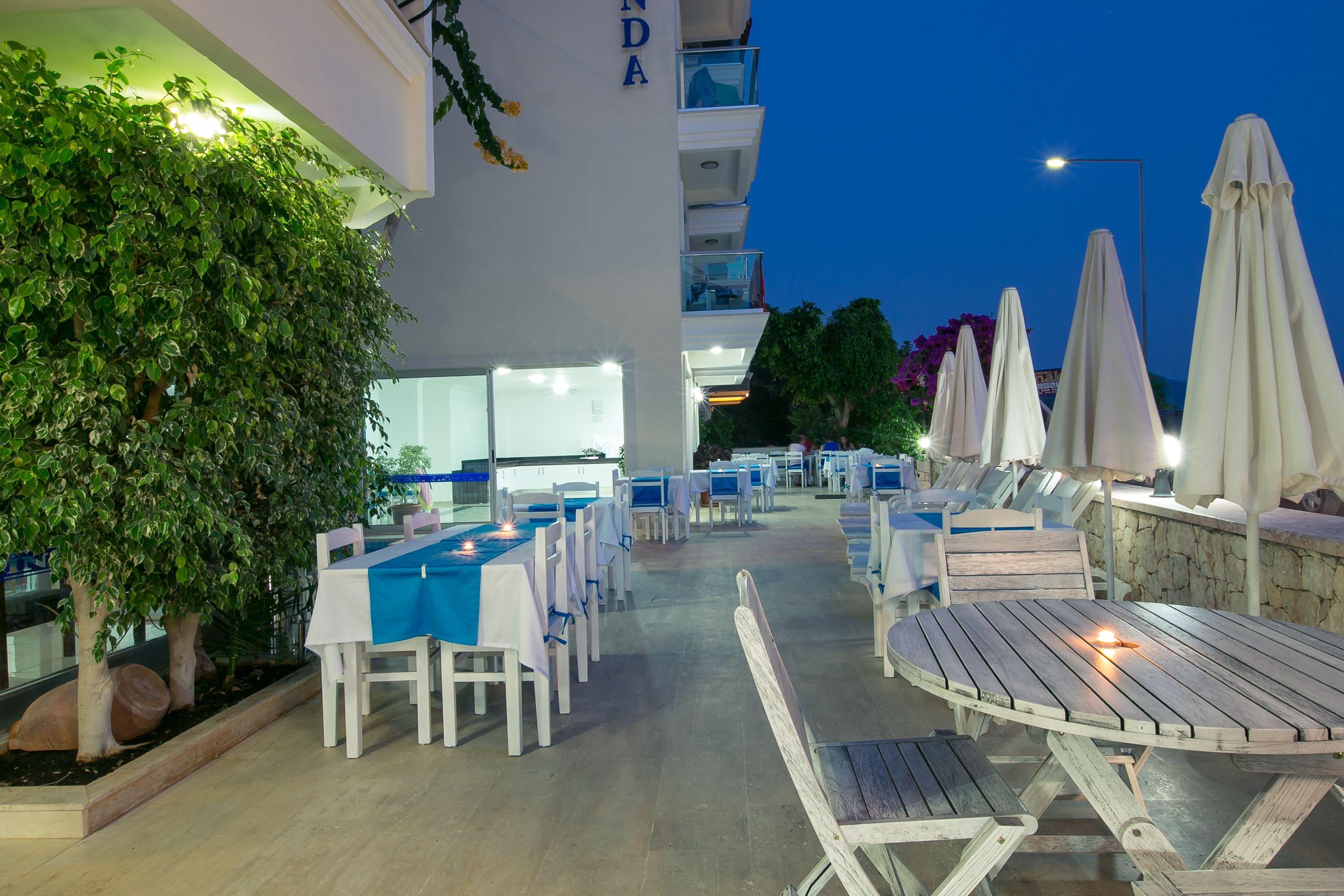 An outdoor dining area with tables and chairs, surrounded by greenery and umbrellas.