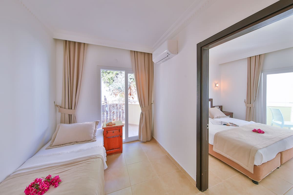 A hotel room with two beds, a small table, a nightstand, and a balcony with curtains.