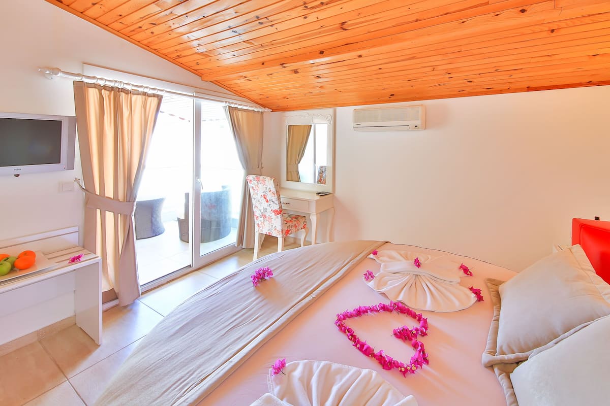 A bedroom with a bed, a desk, a chair, a television, and a sliding glass door to a balcony.