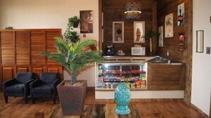 A reception area with wooden paneling, a reception desk, a glass display case, two chairs, and a potted plant. - Hotel Fazenda São Matheus (Serra Negra)