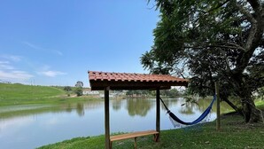 A wooden bench under a tiled roof near a calm lake, with a hammock hanging nearby. - Hotel Fazenda São Matheus (Serra Negra)