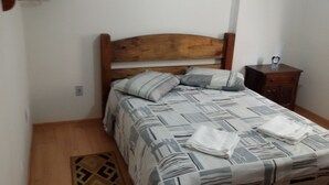 A small, neatly made bed with a wooden headboard, a bedside table with a clock, and a patterned bedspread.
