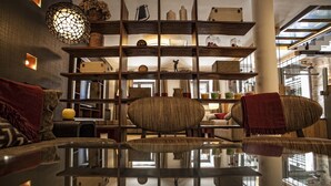 A modern interior with a glass table reflecting the room, wooden shelving with various items, and a cozy seating area with cushions. - Hotel Pura Vida (Valganon)