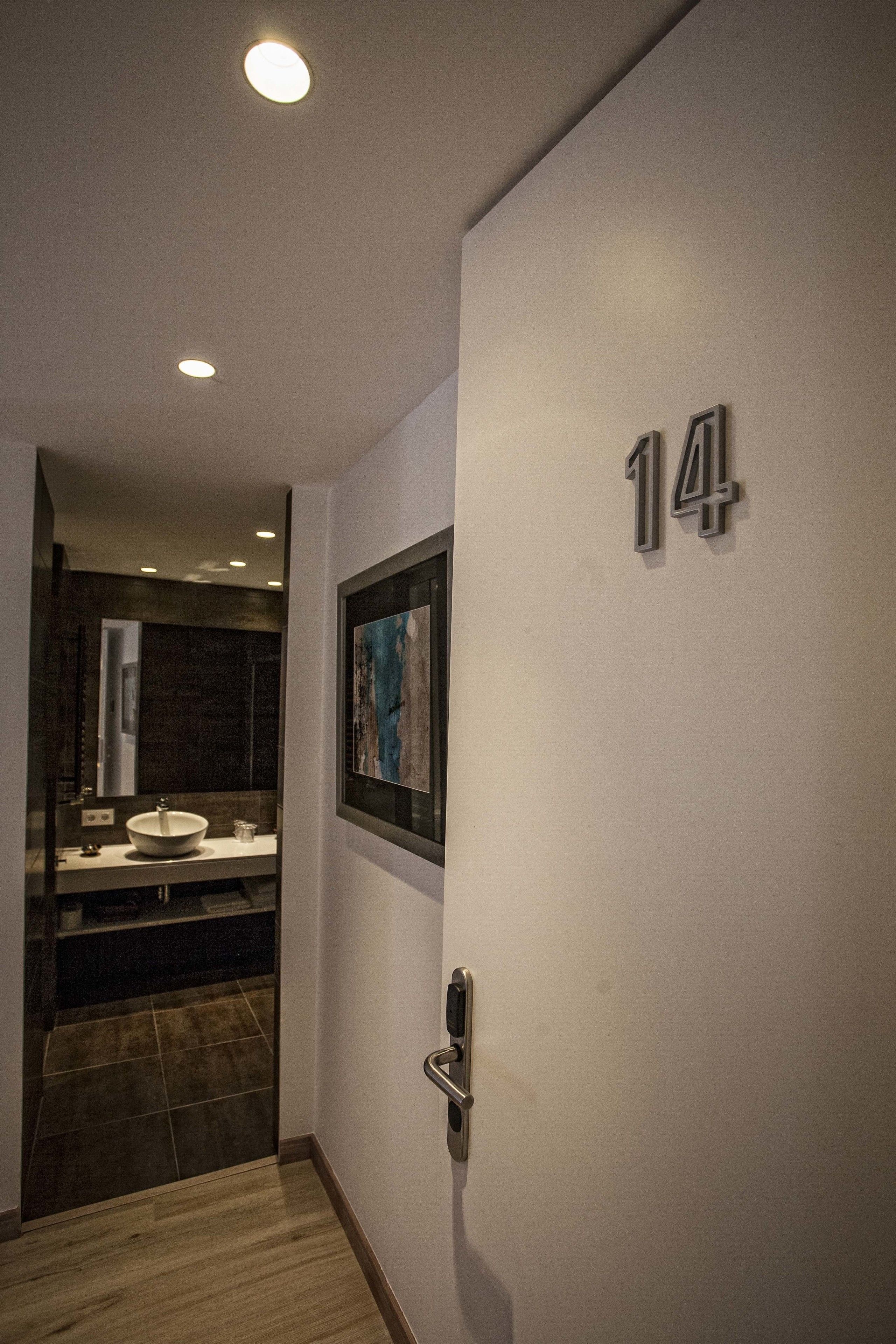 Ein Flur mit der Nummer 14 an der Wand, einem gerahmten Bild und einem modernen Badezimmer mit Waschbecken und Spiegel.
