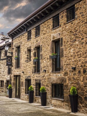 A stone building with multiple windows, some with plants. A sign indicates it is a hotel. - Hotel Pura Vida (Valganon)