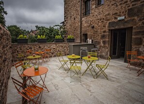 An outdoor patio with stone walls, multiple tables and chairs, and potted plants. - Hotel Pura Vida (Valganon)
