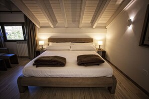 A bedroom with a wooden bed, two bedside lamps, and a view of the outdoors through a window. - Hotel Pura Vida (Valganon)