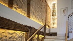 A staircase with stone walls and wooden beams, leading to a landing with a modern light fixture. - Hotel Pura Vida (Valganon)