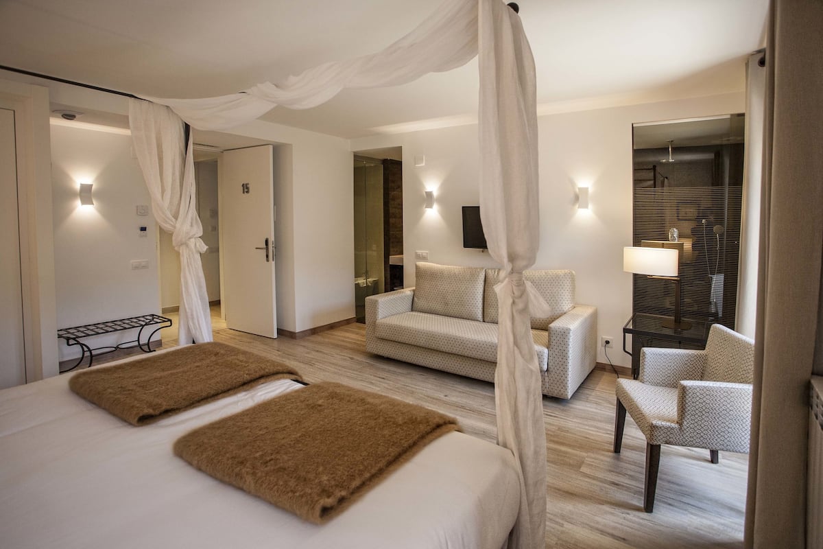 A bedroom with a bed, a sofa, a chair, a mirror, and a television.