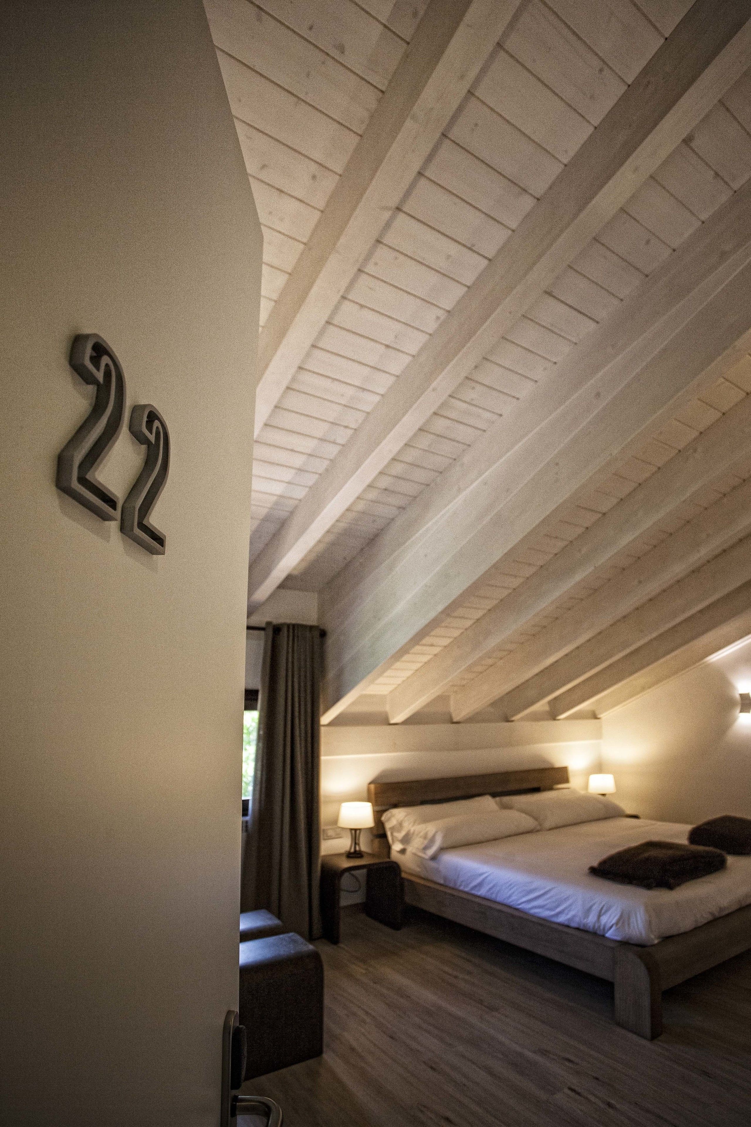 Un dormitorio con techo inclinado, una cama con almohadas, una mesita de noche y un número '22' colgado en la pared.