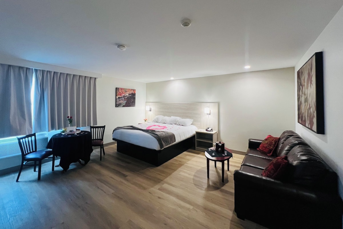 A modern hotel room with a bed, a desk, a chair, a leather sofa, and a nightstand.