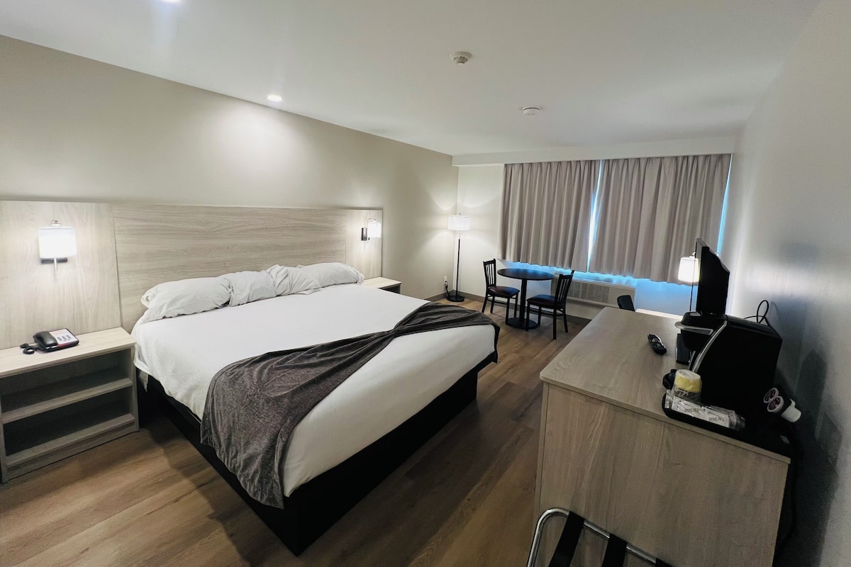 A hotel room with a bed, bedside table, lamp, desk, chair, and a TV.