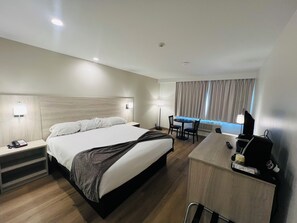 A hotel room with a bed, bedside table, lamp, desk, chair, and a TV. - Pinewood Motor Inn (Espanola)