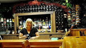 Una zona de bar con un cantinero, estantes llenos de botellas y una barra de madera.