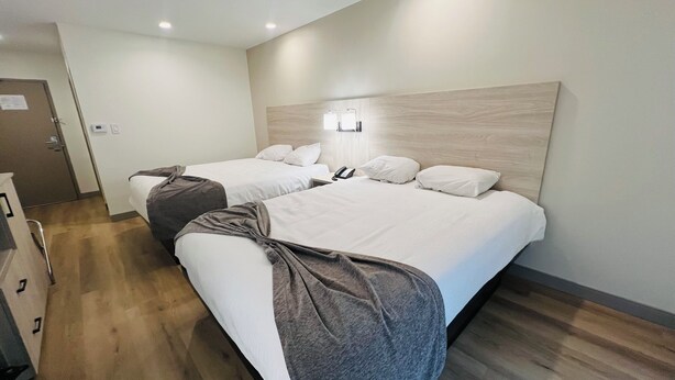 Habitación de hotel con dos camas, suelo de madera, lámpara de pared y una puerta con un cartel.