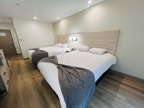 A hotel room with two beds, a wooden floor, a wall-mounted light, and a door with a sign.