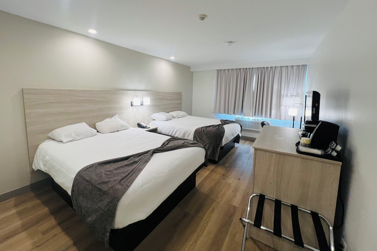 A hotel room with two beds, a desk with a coffee machine, and a chair.