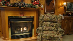 Una chimenea de madera con un letrero de precaución, un sillón floral y un mueble de madera con un teléfono.