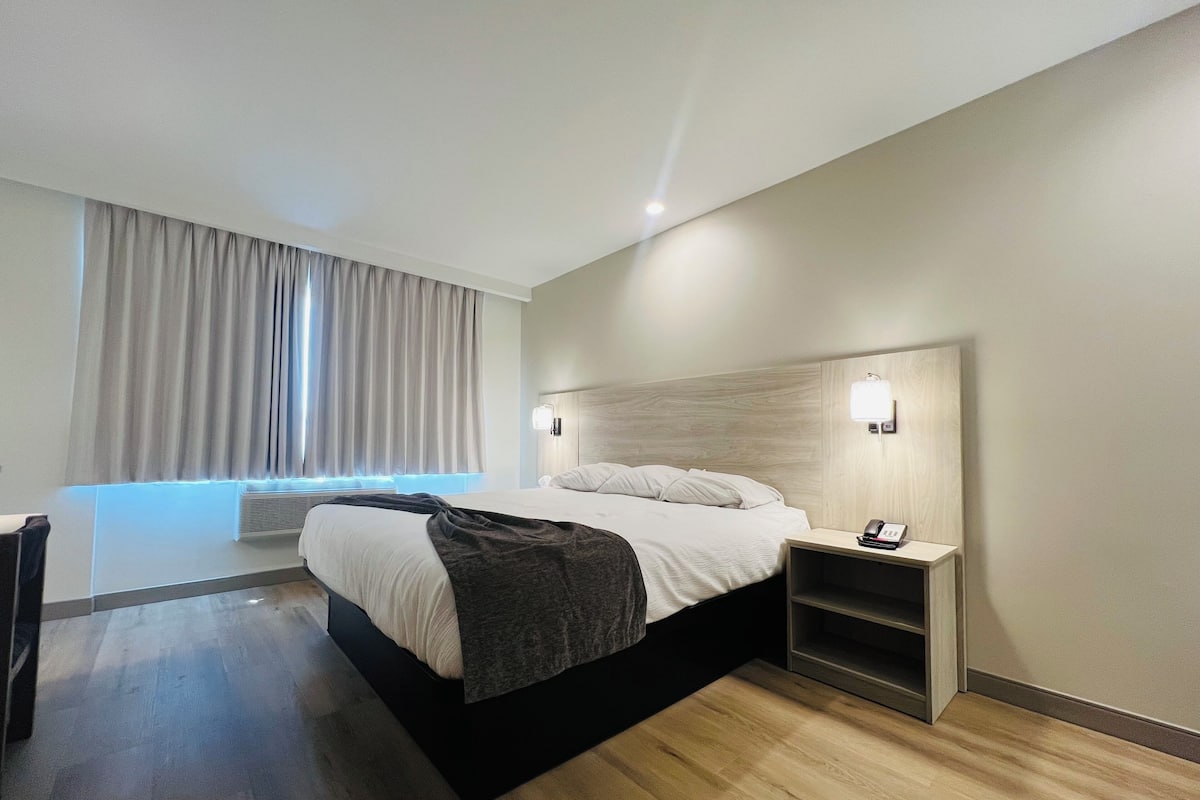 A modern hotel room with a large bed, a bedside table with a phone, and a window with curtains.